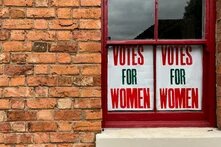 Rotes Backsteingebaude mit zwei Schildern am Fenster "Votes for Women"